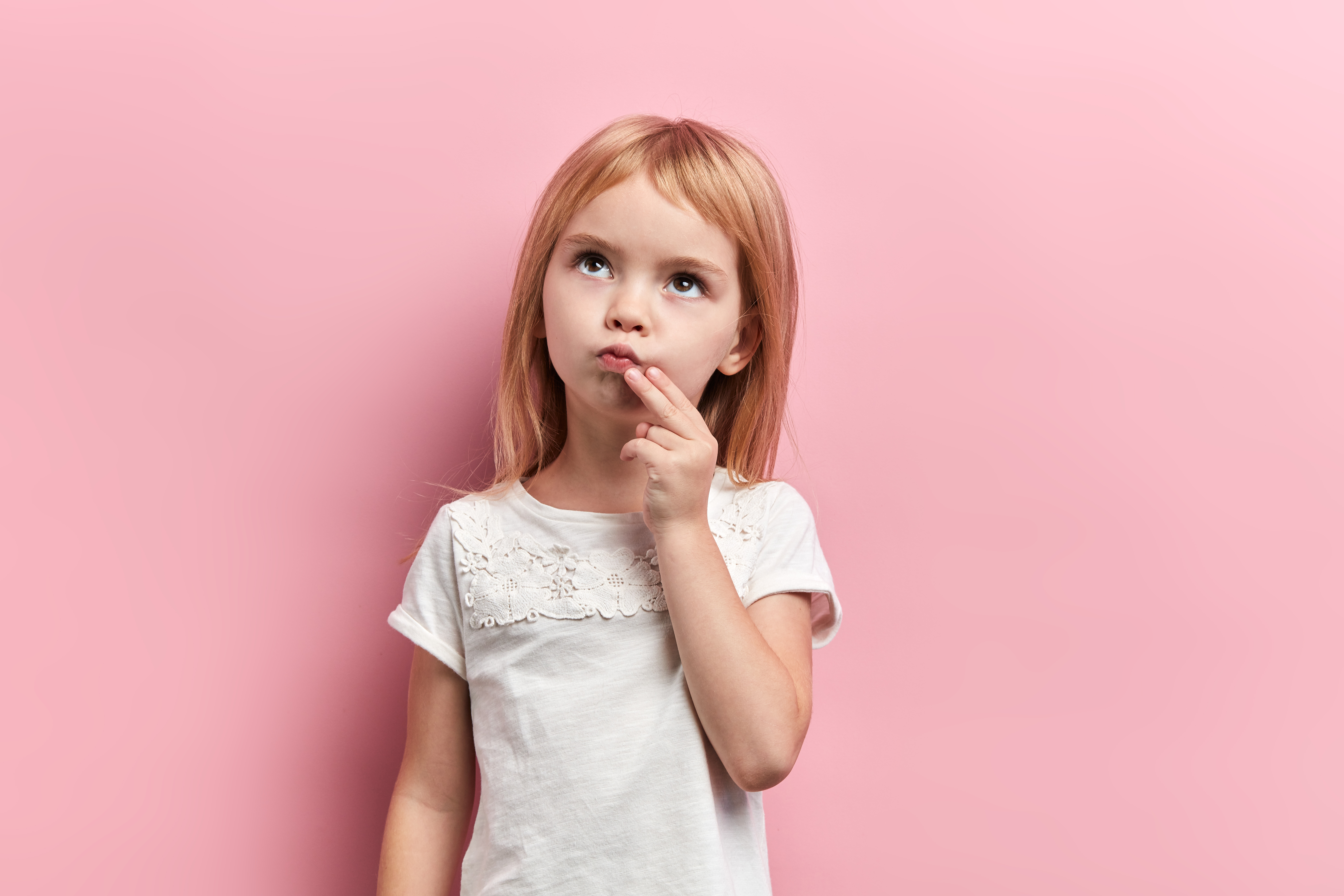 serious pensive girl with a finger on her chin looking up, close up photo. isolated pink background, idea, plan , faciala expression, reaction