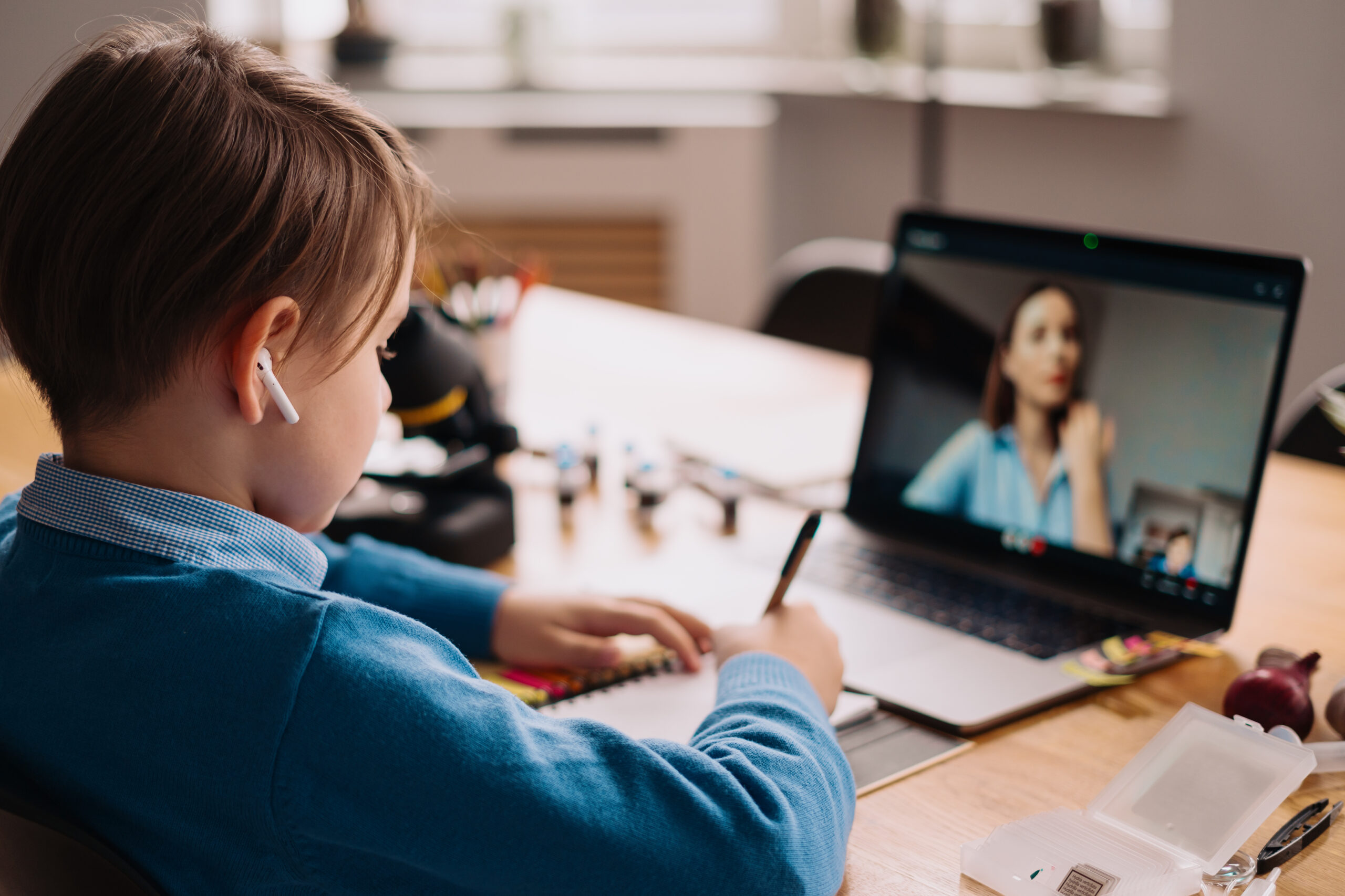 A Preteen boy uses a laptop to make a video call with his teacher. The Screen shows an online lecture with a teacher explaining the subject from class.